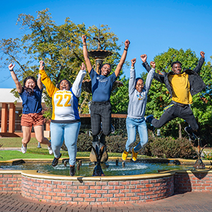 Five students captured mid jump in front of the fountain on campus