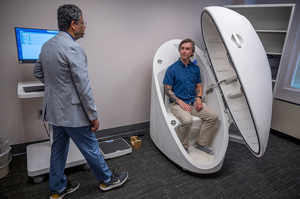 Medical technician analyzes data from BodPod with man inside looking out window