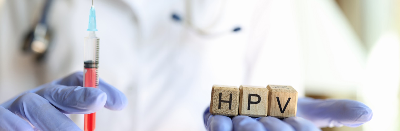 nurse holds needle and blocks that spell out "HPV"