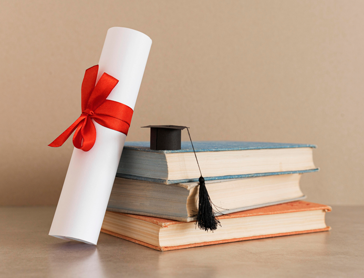 diploma next to books with a small graduation cap on top