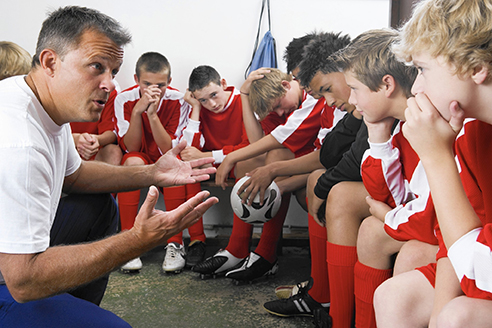 A male sports coach squats down to huddle up with his team and strategize.