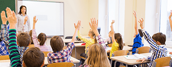 Students raising their hands in a classroom with teacher in the front