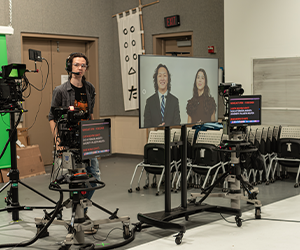 A student filming two students on screen