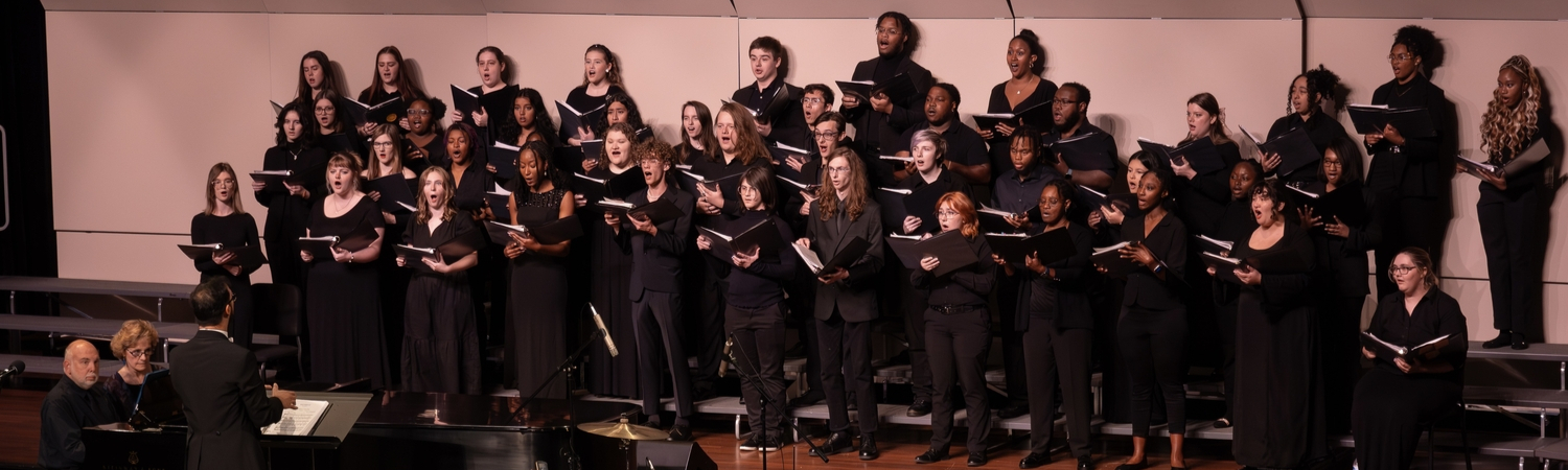 Dr. Marcel Ramalho directs a choral ensemble in 2024. Photo shows students dressed in black arranged on a platform singing.