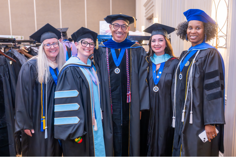 four women and one man standing together wearing graduation robes
