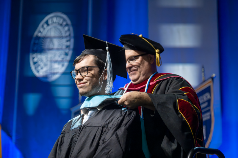 man placing hood on student