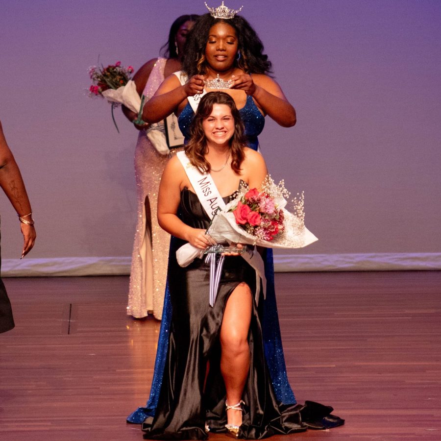 Young woman in an evening gown getting crowned as she holds bouquet of flowers