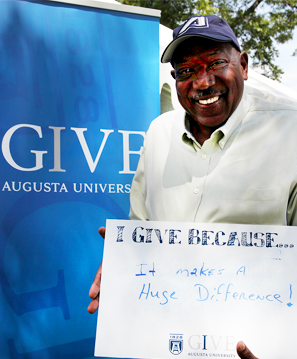 Coach Bryant holding "I give because" sign