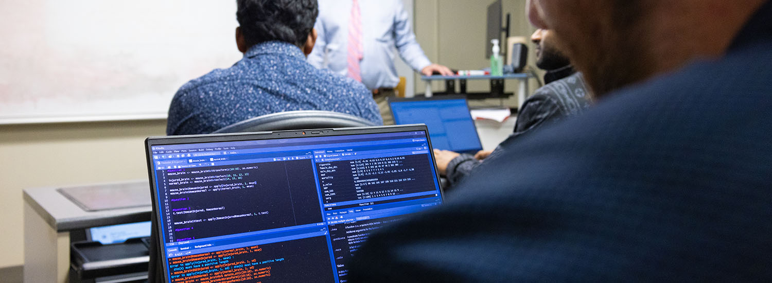 Classroom with student on computer and teacher teaching