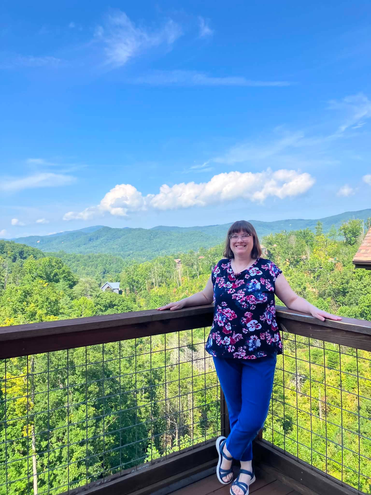 woman with glasses stands on mountain balcony