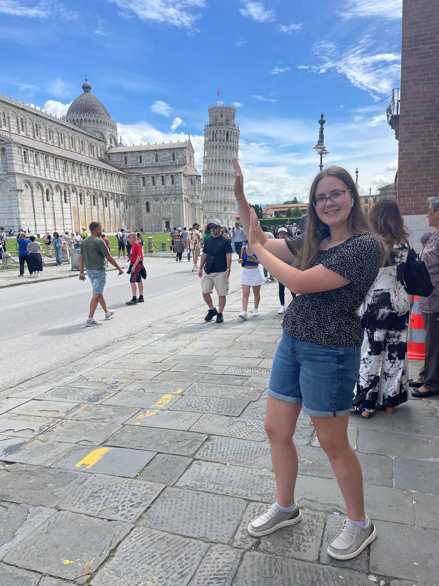 girl stands in front of leaning tower of piza with hands held up