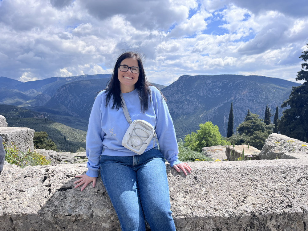 woman in glasses sits in front of a scenic mountain overlook