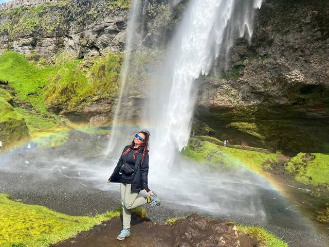 woman stands in front of waterfall with rainbow in background